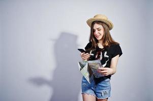 chica turista con mapa, vestida con camisa jajaja, pantalones cortos y sombrero hablando por teléfono móvil aislado en blanco. foto