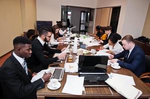 Multiracial business team addressing meeting around boardroom table, working together and write something on papers. photo