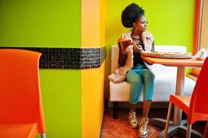 mujer africana con pizza sentada en un restaurante de colores brillantes. foto