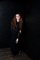 Studio shoot of girl in black with dreads, at glasses and hat on brick background. photo