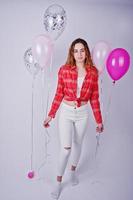 Young girl in red checked shirt and white pants with balloons against white background on studio. photo