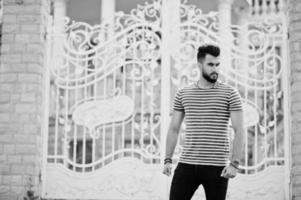 Handsome tall arabian beard man model at stripped shirt posed outdoor against royal iron gates. Fashionable arab guy. photo