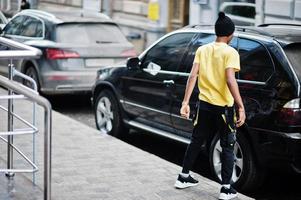 desgaste de hombre africano en sombrero negro posado al aire libre contra el coche de negocios. foto