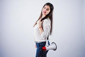 Portrait of a young woman in blue trousers and white blouse posing with megaphone in the studio. photo