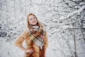 retrato de chica rubia con gafas, abrigo de piel rojo y bufanda en el día de invierno. foto