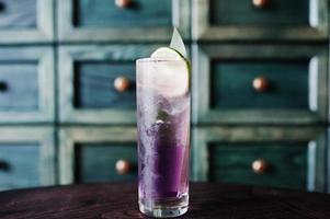 Alcoholic long violet cocktail with ice in glass at bar table. photo
