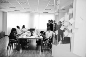 el equipo de negocios multirracial se dirige a la reunión alrededor de la mesa de juntas y escribe el plan a bordo. foto