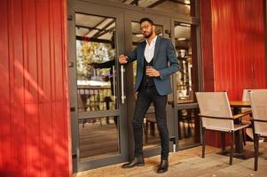 Handsome well-dressed arabian man smoke cigar with glass of whiskey at balcony of pub. photo