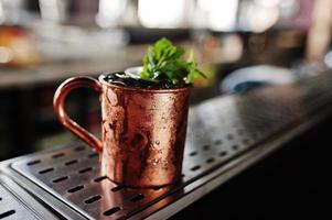 Alcoholic cocktail with ice, mint and lime in bronze cup on bar table. photo