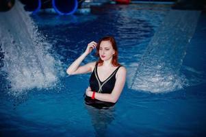 sexy chica pelirroja en traje de baño negro descansando en la piscina del parque acuático. foto