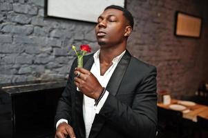 Strong powerful african american man in black suit sniff flower in test tube against piano.