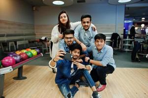 Group of five south asian peoples having rest and fun at bowling club. Making selfie by phone. photo