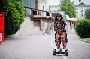 hermosa mujer afroamericana usando segway o hoverboard. chica negra en scooter eléctrico autoequilibrado de doble rueda. foto