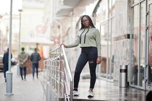 City portrait of positive young dark skinned female wearing green hoody and eyeglasses. photo