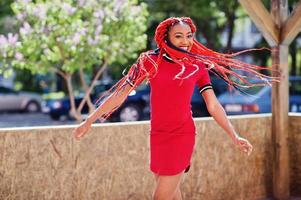 Cute and slim african american girl in red dress with dreadlocks in motion having fun on street. Stylish black model. photo