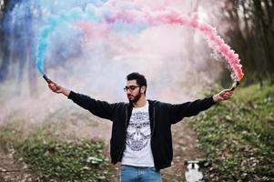 Street style arab man in eyeglasses hold hand flare with red and blue smoke grenade bomb. photo