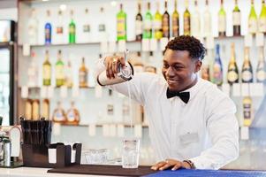 camarero afroamericano en el bar con agitador. preparación de bebidas alcohólicas. foto