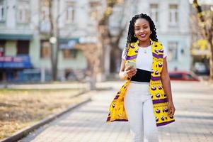 Stylish african american women in yellow jacket posed on street at sunny day with mobile phone at hand. photo