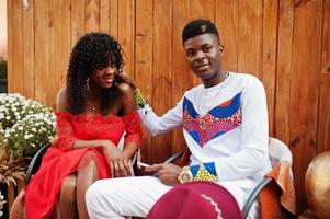 elegante pareja afro francia de moda posaron juntos en el día de otoño. modelos africanos negros enamorados sentados contra una decoración de madera con flores y calabazas. foto