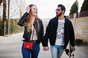 Cool multiracial couple walking together with longboard. photo