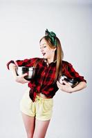 Young funny housewife in checkered shirt and yellow shorts pin up style with two saucepan isolated on white background. photo