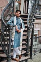 hombre indio vestido con ropa tradicional con bufanda blanca posada al aire libre contra escaleras de hierro. foto
