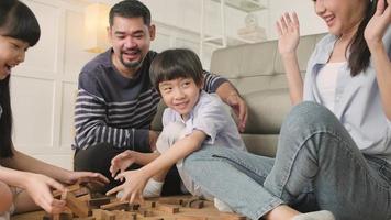 Happy Asian lovely Thai family activity, parents, dad, mum, and children have fun playing and joyful wooden toy blocks together on living room floor, leisure weekend, and domestic wellbeing lifestyle. video