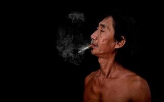 el anciano delgado del retrato estaba fumando en el fondo negro, la imagen del humo del cigarrillo esparcido en el concepto de la boca foto