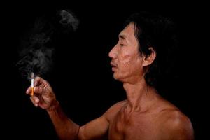 el anciano delgado del retrato estaba fumando en el fondo negro, la imagen de la mano de los hombres sosteniendo el humo del cigarrillo esparcido en el concepto de la boca foto