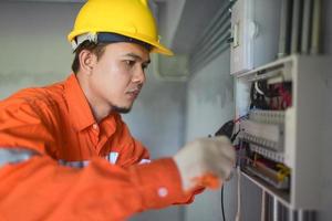 Side view of a handsome Asian electrician repairing an electrical box with pliers in the corridor. photo