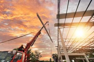 Workers install new roofs using mobile cranes. Raise the metal roof sheet on the ceiling frame. Go up to store above the steel frame roof at the construction project. photo