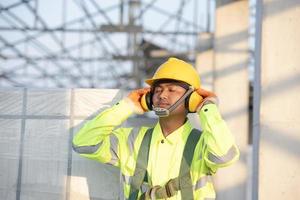 ingenieros asiáticos en cascos de seguridad y chalecos de seguridad para trabajadores con auriculares protectores en obras de construcción. foto