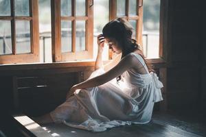 triste mujer asiática con vestido blanco que sufre depresión insomnio despierta y se sienta sola en la cama en un dormitorio antiguo. acoso sexual y violencia contra la mujer.
