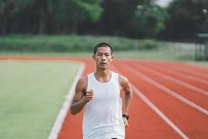 Athlete sportman runner training run on lane at the stadium in morning. Runner man wearing white vest to practice running prepare for competition race. Sport concept. photo