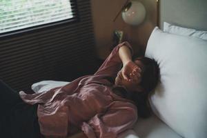 triste mujer asiática que sufre depresión insomnio despierta y se sienta sola en la cama en el dormitorio. acoso sexual y violencia contra la mujer, concepto de salud foto