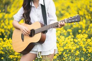 Asian young woman playing guitar and sing music in the park, asian woman palying guitar at yellow flowers garden photo