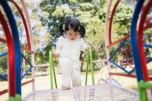 linda chica asiática juega en la escuela o en el jardín de infantes o en el patio de recreo. Actividad de verano saludable para niños. niña asiática escalando al aire libre en el patio de recreo. niño jugando en el patio de recreo al aire libre. foto