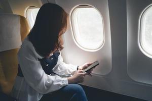 Asian woman sitting in a seat in airplane and using mobile phone by the window and going on a trip, asian woman passenger is leaving for a trip by plane on vacation. Vacation travel concept. photo