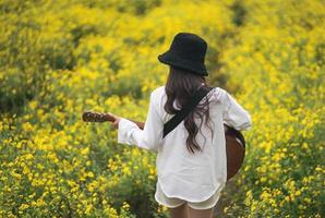 mujer joven asiática tocando la guitarra y cantando música en el parque, mujer asiática tocando la guitarra en el jardín de flores amarillas foto