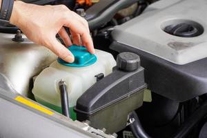 el mecánico inspecciona el tanque de expansión con anticongelante verde. nivel de refrigerante del vehículo en el sistema del radiador del automóvil. autopartes foto