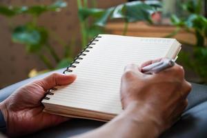 young man hand writing blank notebook on wooden table hill in the morning tree background photo