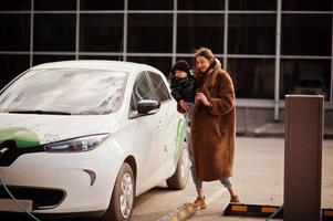 Young mother with child charging electro car at the electric gas station. photo