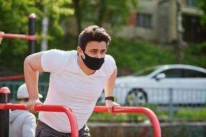 Portrait sports arabian man in black medical face mask doing workout exercises in outdoor gym place during coronavirus quarantine. photo