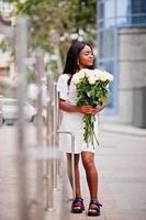 Beautiful african american girl holding bouquet of white roses flowers on dating in the city. Black businesswoman with bunch of flowers. photo