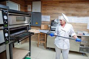 Female chef preparing pizza in restaurant kitchen. photo
