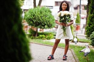 Beautiful african american girl holding bouquet of white roses flowers on dating in the city. Black businesswoman with bunch of flowers. photo