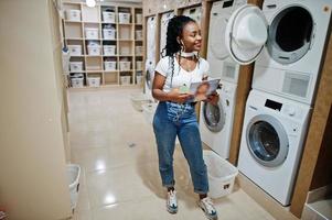 alegre mujer afroamericana cerca de la lavadora en la lavandería de autoservicio. foto