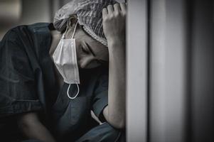 Tired depressed female asian scrub nurse wears face mask blue uniform sits on hospital floor,Young woman doctor stressed from hard work photo