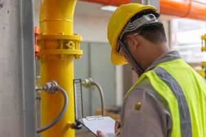 Asian engineer wearing glasses working in the boiler room,maintenance checking technical data of heating system equipment,Thailand people photo