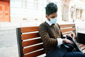 Coronavirus covid-19 concept. South asian indian man wearing mask for protect from corona virus sitting on bench. photo